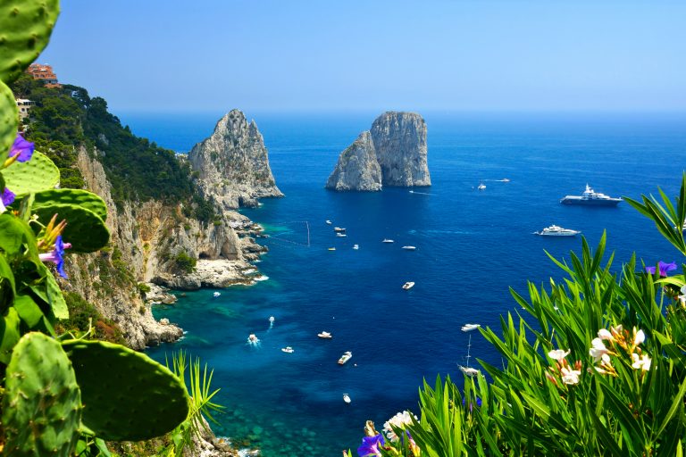 Capri coast view with the Faraglioni rocks, flowers and boats in the blue sea, Italy